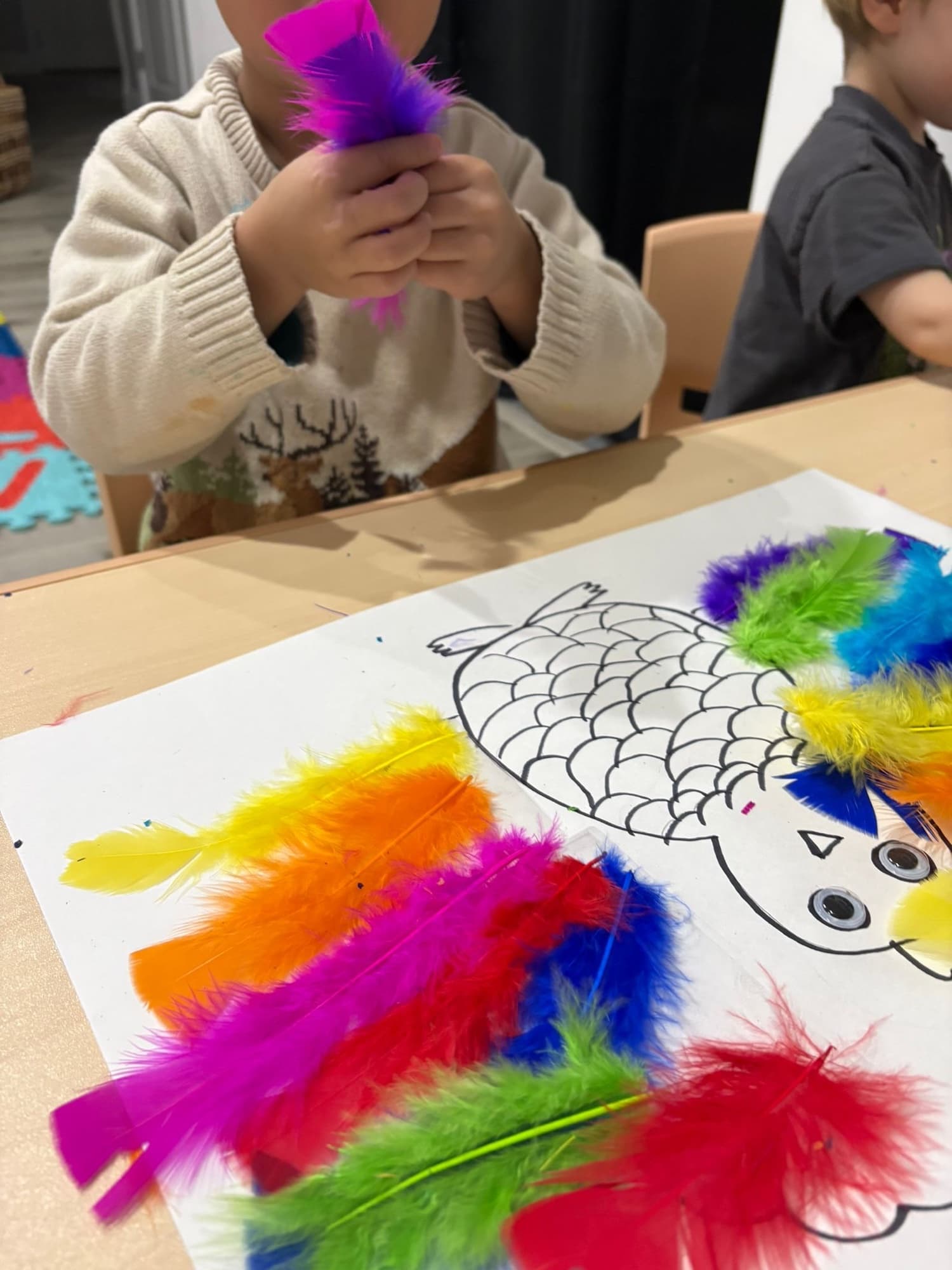 Small hands gluing colorful feathers onto a craft project